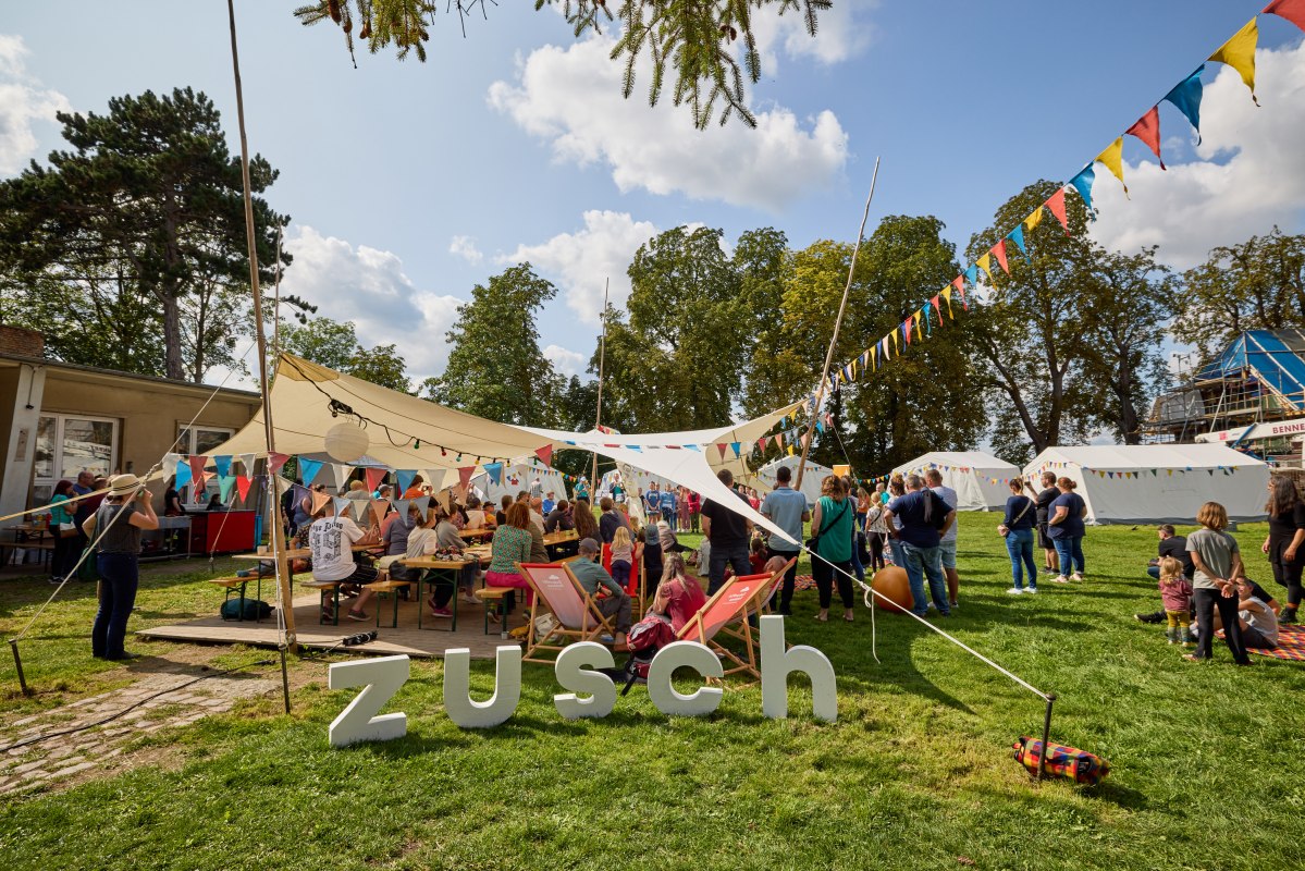 Mensen staan onder een luifel versierd met kleurrijke wimpels // &copy; Oliver Borchert