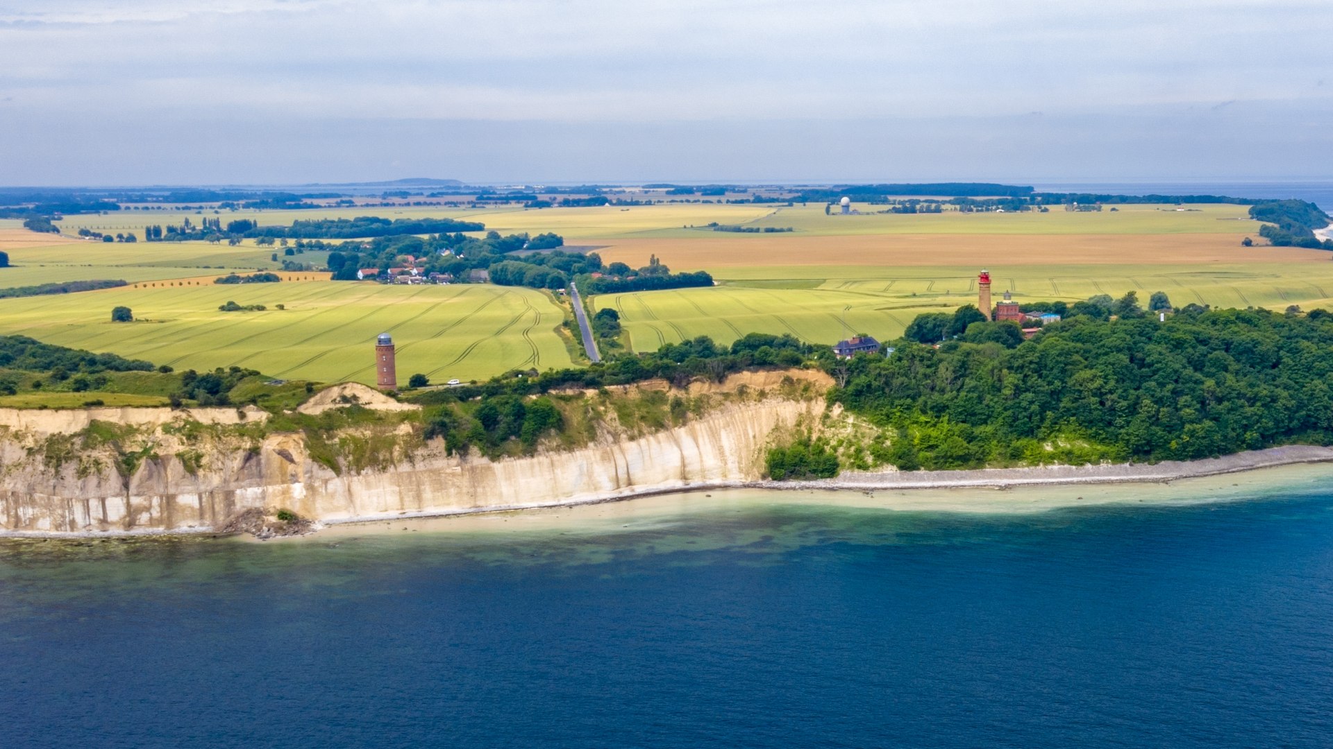 Luchtfoto van de krijtrotsen bij Kaap Arkona op het eiland Rügen. Op de achtergrond strekken velden en de Baltische Zee zich uit onder een heldere hemel.