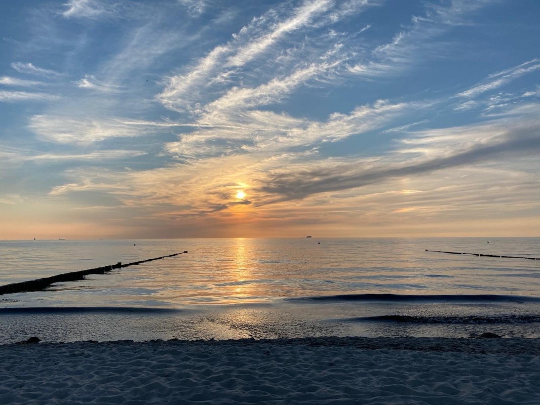 De foto toont de spiegelgladde Oostzee, waarvan het kalme wateroppervlak de kleuren van de zonsondergang weerspiegelt. De lucht is hier en daar lichtblauw, afgewisseld met fijne wolkenstrepen die het panorama een zachte dynamiek geven. Een vredig strand strekt zich uit langs de rand van het motief en nodigt de kijker uit om te blijven hangen. De sfeer is kalm en harmonieus, alsof de wereld even pauzeert om te genieten van de schoonheid van het moment. // © byc De foto toont de spiegelgladde Oostzee, waarvan het kalme wateroppervlak de kleuren van de zonsondergang weerspiegelt. De lucht is hier en daar lichtblauw, afgewisseld met fijne wolkenstrepen die het panorama een zachte dynamiek geven. Een vredig strand strekt zich uit langs de rand van het motief en nodigt de kijker uit om te blijven hangen. De sfeer is kalm en harmonieus, alsof de wereld even pauzeert om te genieten van de schoonheid van het moment. // © byc