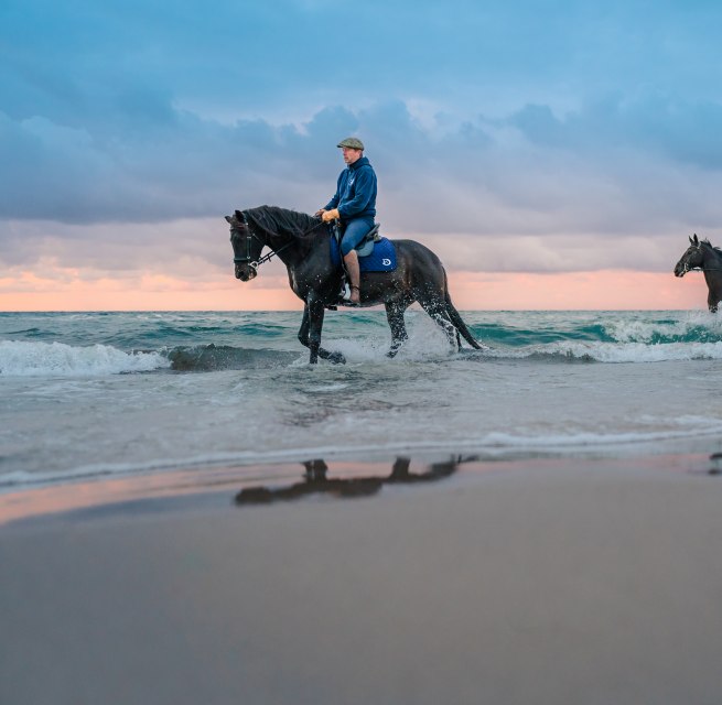 Dwóch jeźdźców na koniach jeździ po plaży o zachodzie słońca nad Morzem Bałtyckim na półwyspie Fischland-Darß-Zingst