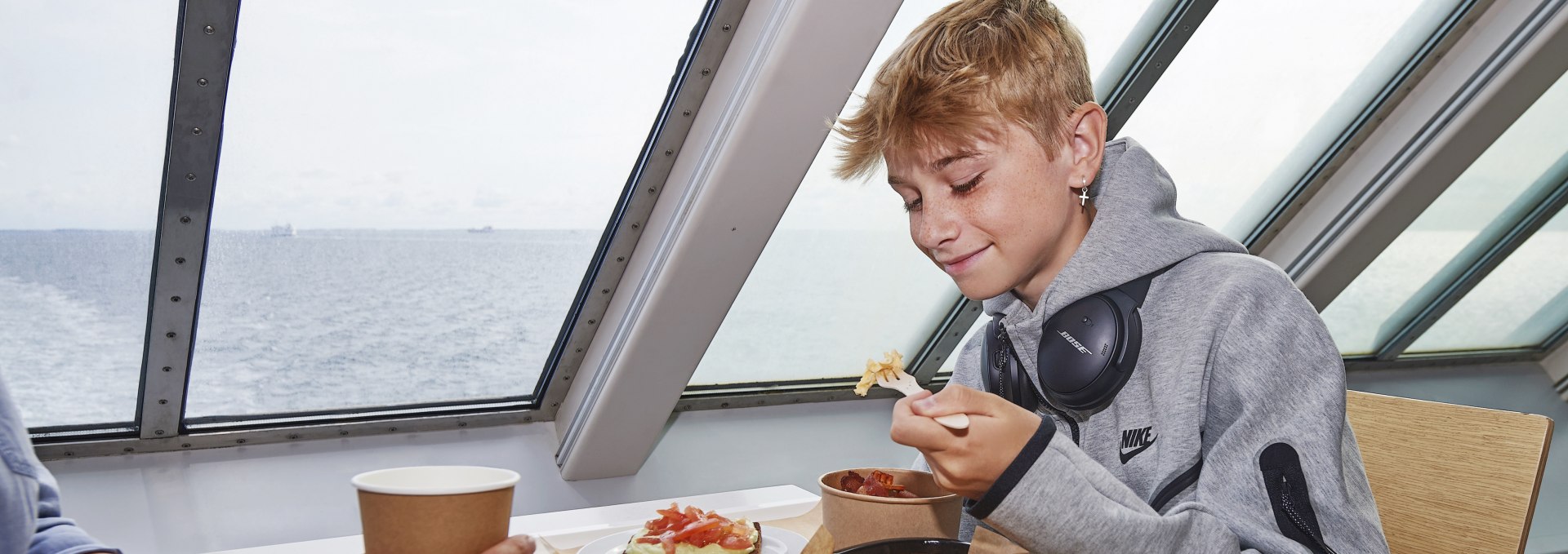 Boy eating snacks on board a Scandlines ferry with a view of the open Baltic Sea through the windows.