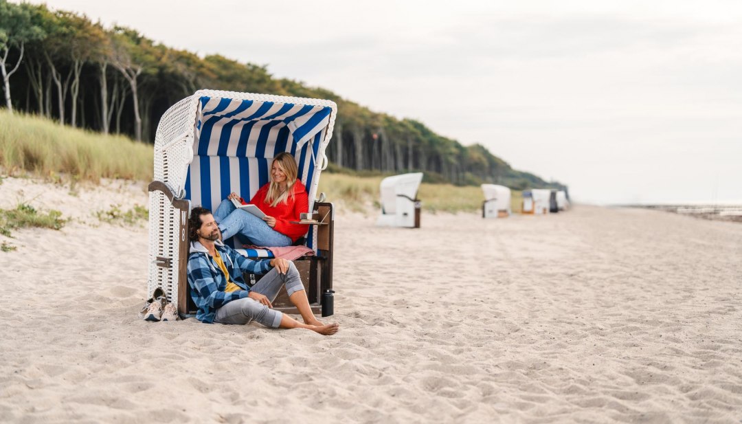 Ett par sitter i en strandkorg p&aring; stranden i Graal-M&uuml;ritz vid &Ouml;stersj&ouml;kusten. I bakgrunden syns kustskogen.