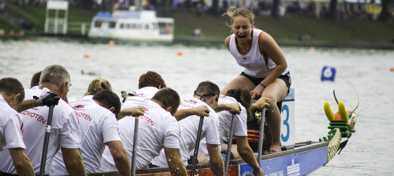 Dragon boat with crew on the Pfaffetneich. A woman sits on the bow, controlling the stroke and calling out to the team., © Niclas Rühl/drachenbootfestival.de