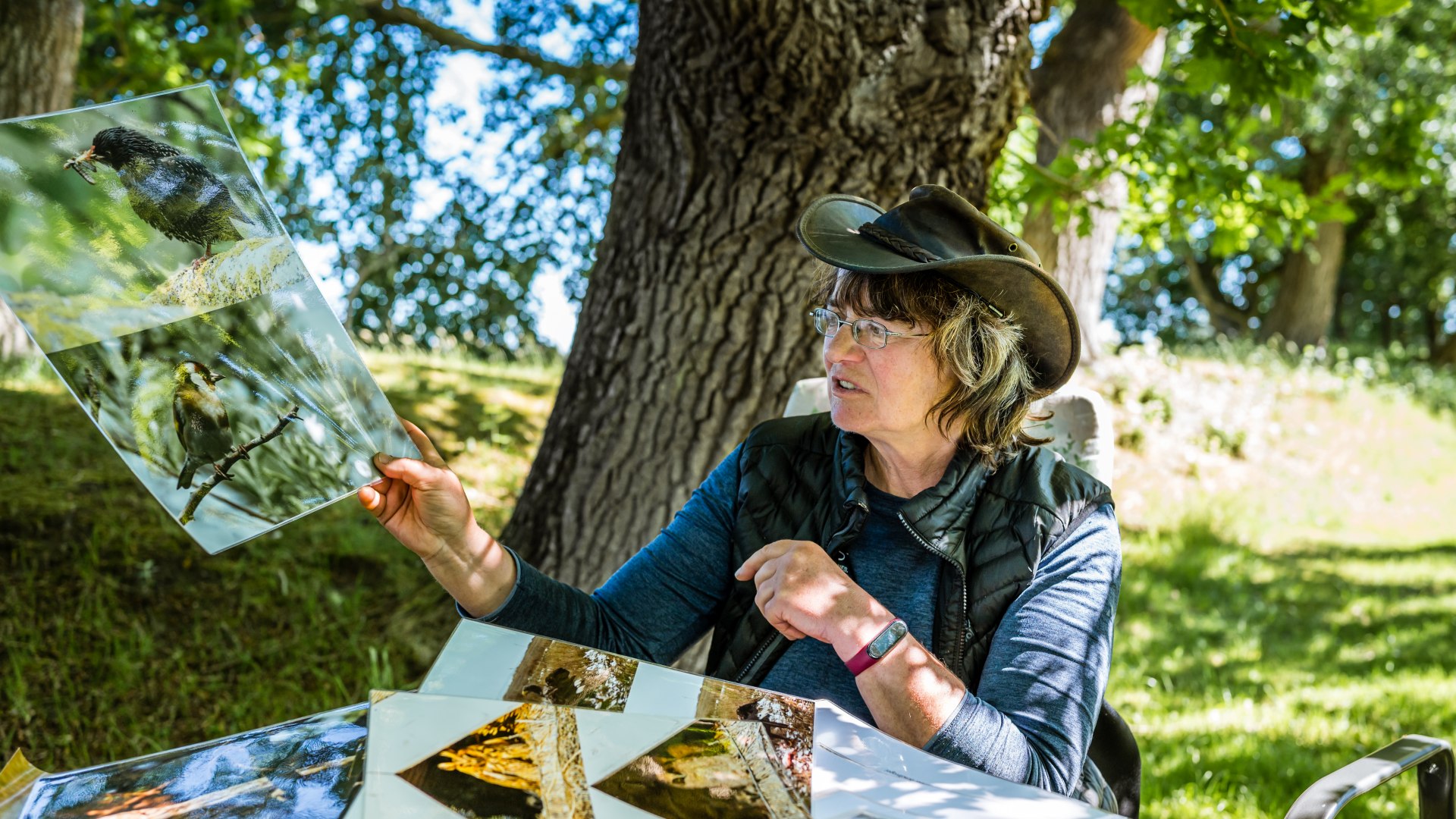 Sylvia Juhnke toont grote, zelfgeschoten vogelfoto's aan een tafel onder een boom.