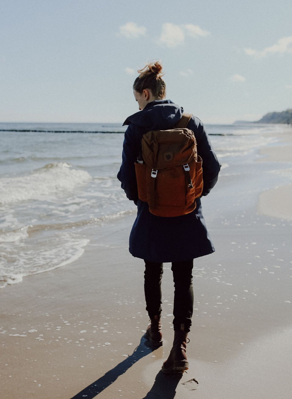 Een wandelaarster wandelt langs de kust van het eiland Usedom terwijl de golven over het strand slaan. Uitgerust met een rugzak gaat ze op zoek naar verborgen schatten zoals barnsteen, dat hier vaak aan de kust te vinden is. // © MV-T/Wanderfolk Een wandelaarster wandelt langs de kust van het eiland Usedom terwijl de golven over het strand slaan. Uitgerust met een rugzak gaat ze op zoek naar verborgen schatten zoals barnsteen, dat hier vaak aan de kust te vinden is.
