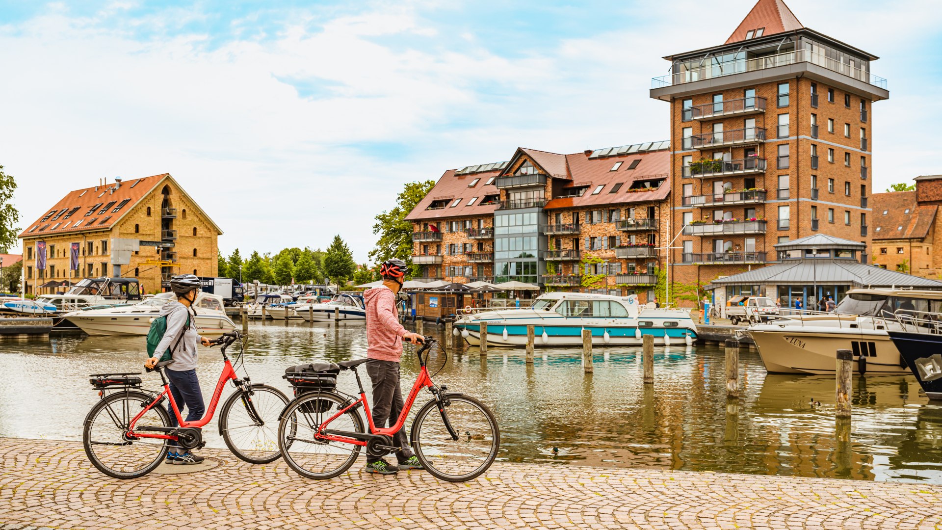 De haven van de koninklijke zetel van Neustrelitz - waar een echtpaar met fietsen staat. // Fietsers en boottoeristen ontmoeten elkaar hier, in de haven van de koninklijke zetel van Neustrelitz // © MV-T/Tiemann De haven van de koninklijke zetel van Neustrelitz - waar een echtpaar met fietsen staat.