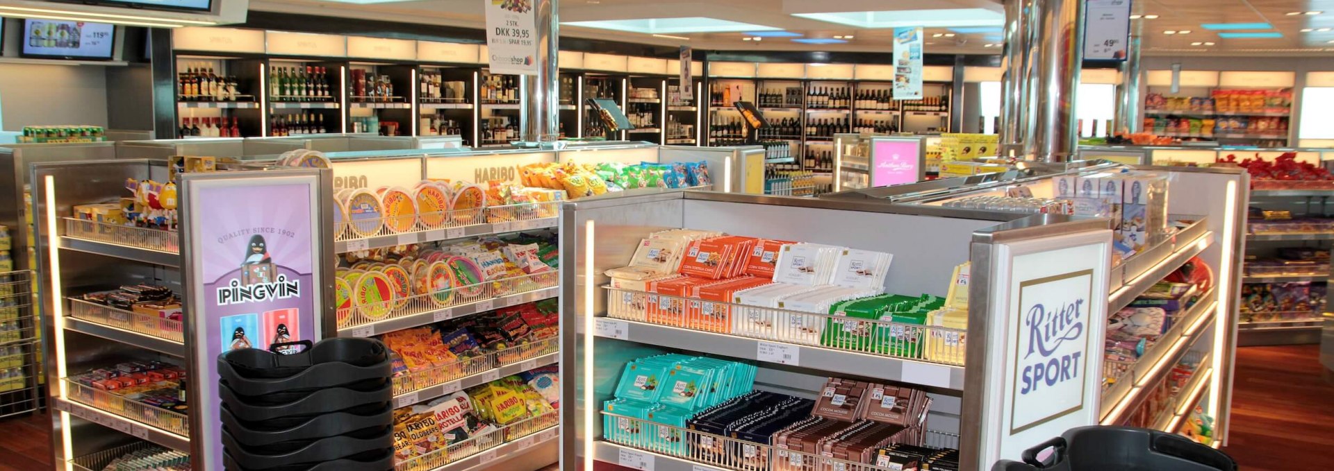 Brightly lit shop on a Scandlines ferry with shelves full of Ritter Sport chocolate, Haribo candy, and duty-free products.
