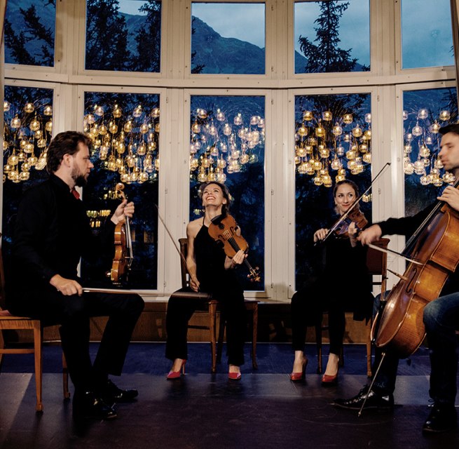 Four musicians with string instruments sit in front of a window wall, © Felix Bröde Four musicians with string instruments sit in front of a window wall, © Felix Bröde