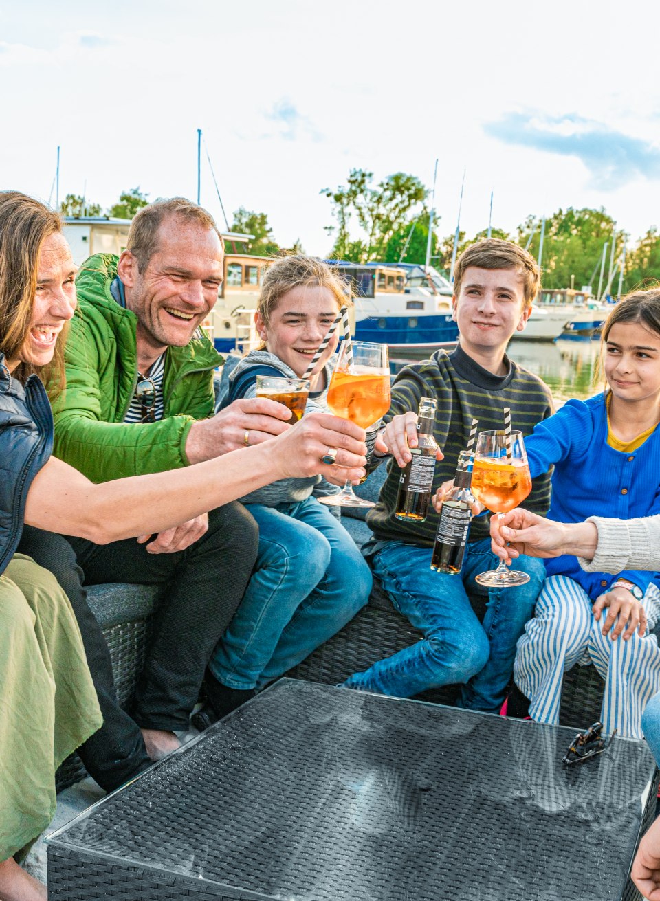 Een heerlijke afsluiting van de dag in Pirate's Bar: de twee vriendelijke families proosten op een geweldige vakantie met hun voeten in het zand., © TMV/Tiemann Twee families klinken glazen in de Pirate's Bar.