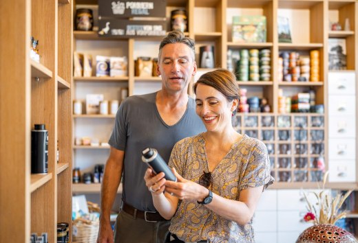 Lachend stel in een boerderijwinkel, omringd door schappen met regionale producten, bekijkt een artikel.