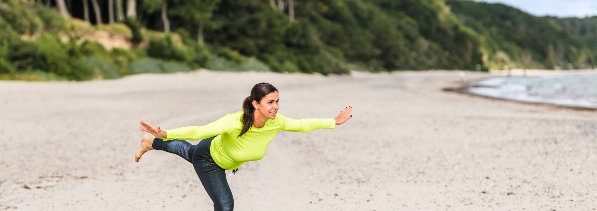 Een vrouw doet de "staande balans" op het strand en houdt haar evenwicht.