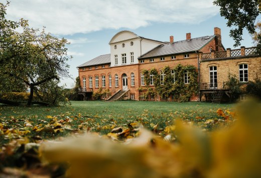 Bakstenen landhuis met wijngaarden en open trappenhuis in een herfstig parklandschap in West-Pommeren onder een licht bewolkte hemel.
