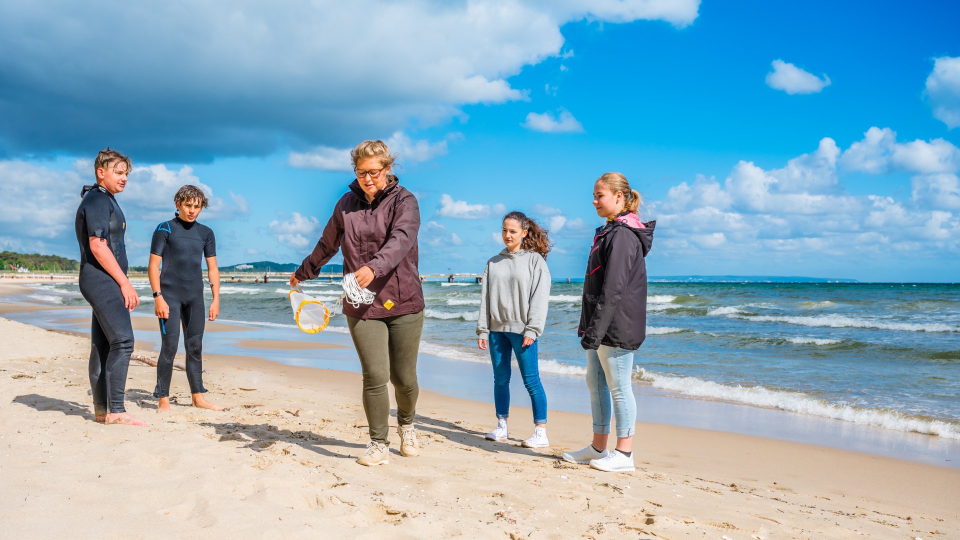 Een mariene biologe toont een klein sleepnet voor het vangen van monsters uit de Baltische Zee. De kinderen om haar heen kijken aandachtig toe.