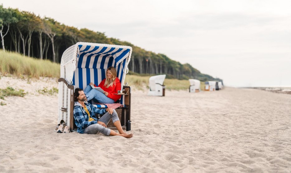 Couple sitting in a beach chair on the beach at Graal-Müritz on the Baltic Sea coast. The coastal forest can be seen in the background. // A couple sits in a beach chair on the beach in Graal-Müritz // © MV-T/Gross Couple sitting in a beach chair on the beach at Graal-Müritz on the Baltic Sea coast. The coastal forest can be seen in the background.