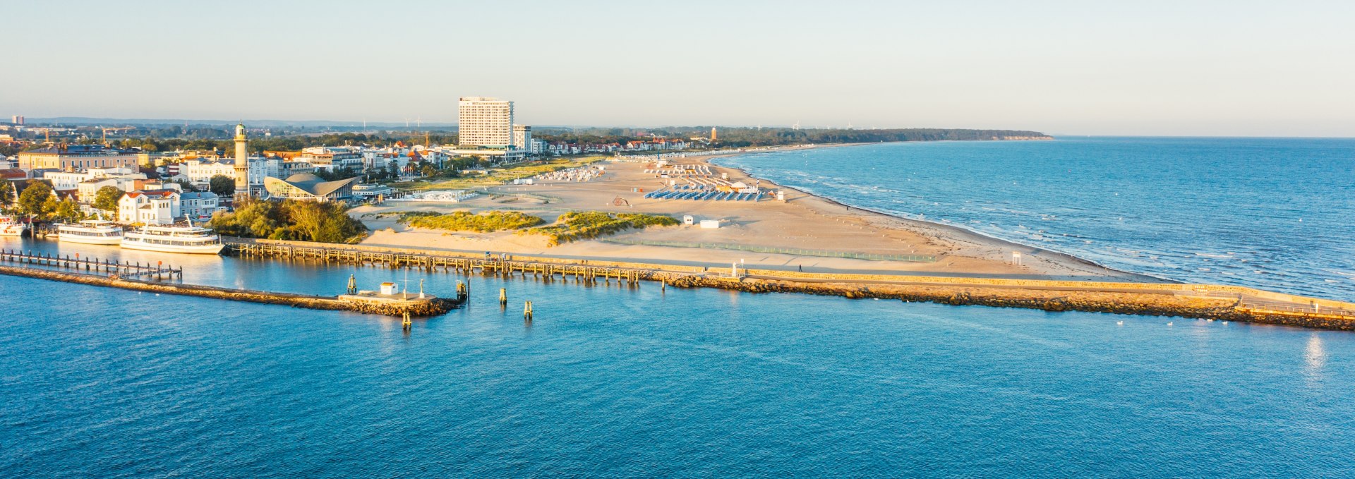 View of the beach and promenade of Warnemünde with lighthouse, hotel and Baltic Sea coast in the evening light.