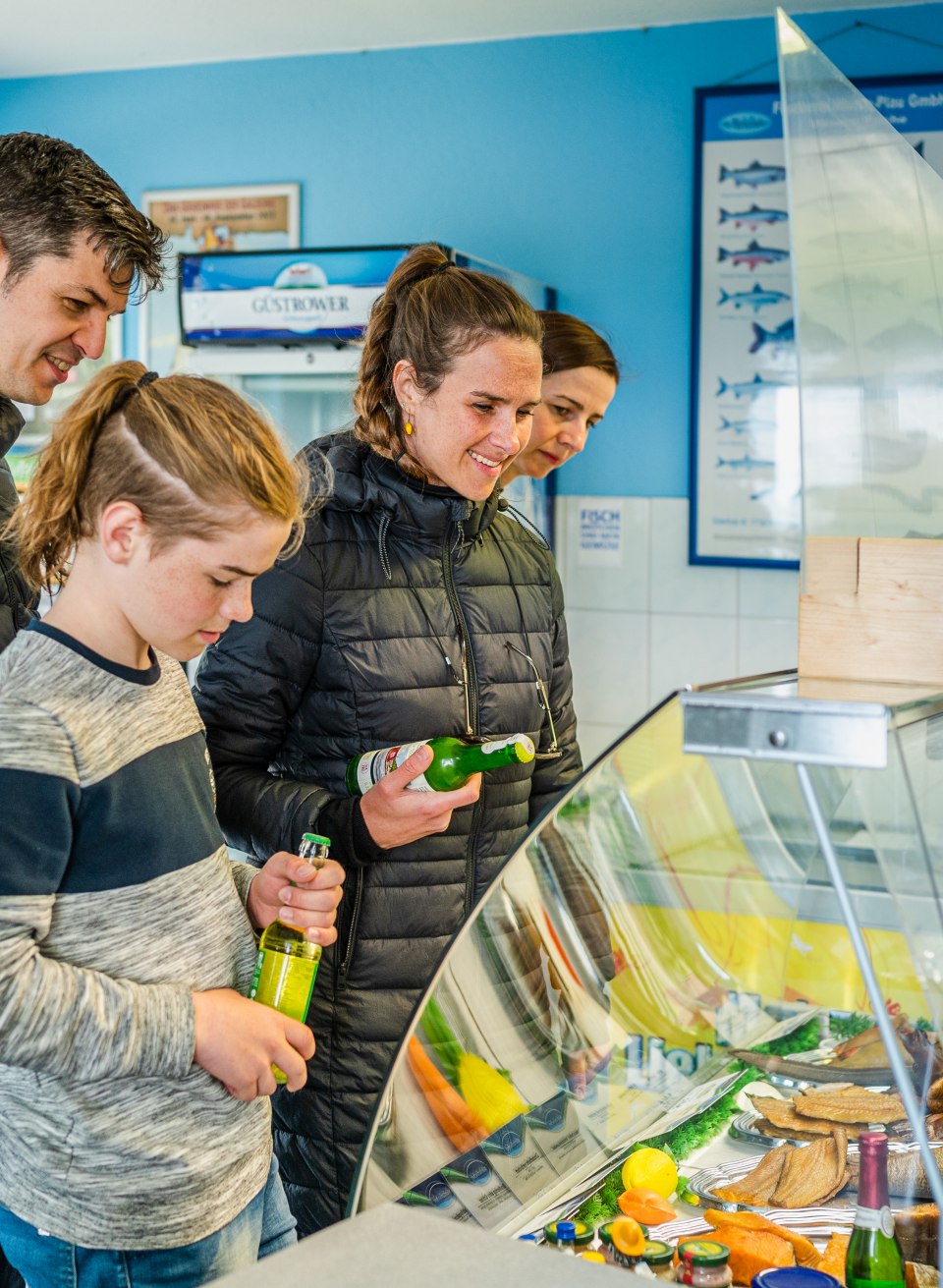Bismarck herring, pike and baked fish in a roll, please: The two families are already regulars at the Fischerhof in Vipperow., © TMV/Tiemann Two families stand at the counter of Fischerhof Vipperow and choose a fish sandwich.