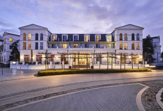 Oświetlony Strandhotel Zingst w stylu architektury uzdrowiskowej o zmierzchu, ujęcie od strony ulicy.