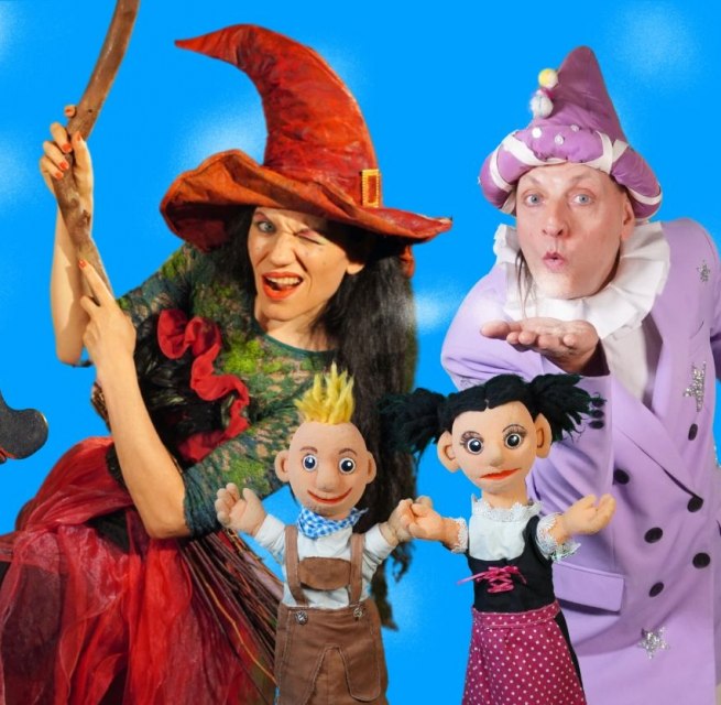 Two puppeteers dressed as a witch and a wizard and two hand puppets Hansel and Gretel in front of a blue background, © Theater Phoebus