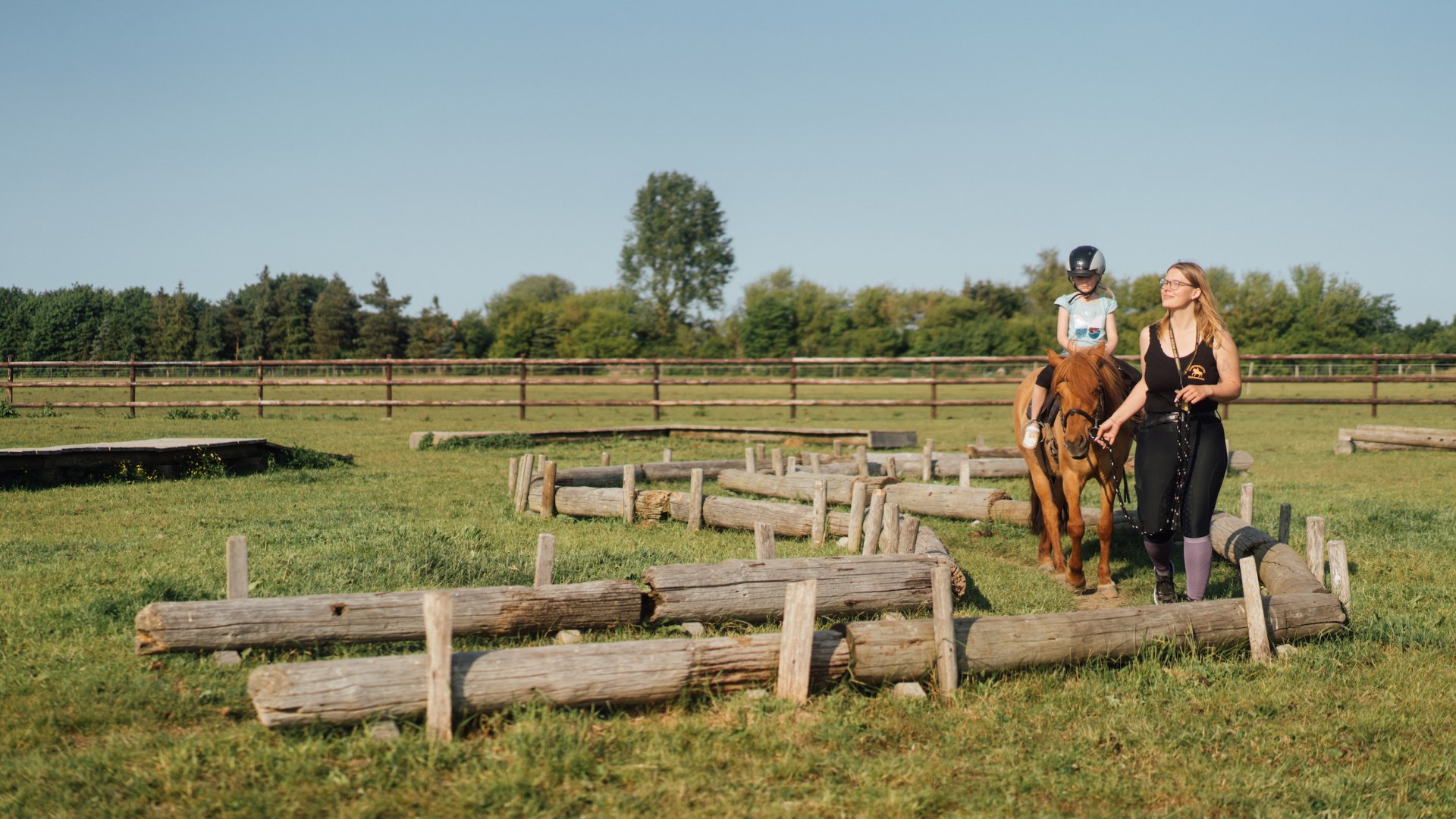 A child sits on a pony and is led by a riding instructor.