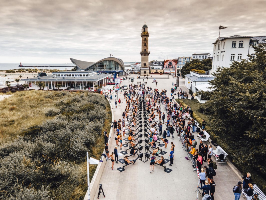 Zawody wioślarskie przed latarnią morską Warnemünde na promenadzie z ergometrami wioślarskimi podczas zawodów fitness Battle The Beach. // © MV-T/Witzel Zawody wioślarskie przed latarnią morską Warnemünde na promenadzie z ergometrami wioślarskimi podczas zawodów fitness Battle The Beach. // © MV-T/Witzel