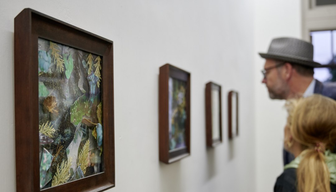 Odwiedzający oglądają oprawione kolaże przyrodnicze na jasnej wystawie podczas serii wydarzeń KUNST HEUTE.