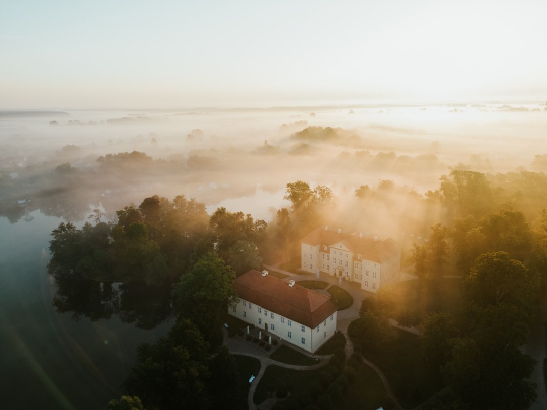 Goldenes Licht taucht Schloss Mirow in eine mystische Atmosphäre. Nebelschwaden ziehen über die Seenlandschaft der Mecklenburgischen Seenplatte und lassen das historische Ensemble aus dem 18. Jahrhundert wie aus der Zeit gefallen wirken. Ein Moment purer Stille zwischen Wasser und Wald. // © 1000seen.de Goldenes Licht taucht Schloss Mirow in eine mystische Atmosphäre. Nebelschwaden ziehen über die Seenlandschaft der Mecklenburgischen Seenplatte und lassen das historische Ensemble aus dem 18. Jahrhundert wie aus der Zeit gefallen wirken. Ein Moment purer Stille zwischen Wasser und Wald. // © 1000seen.de