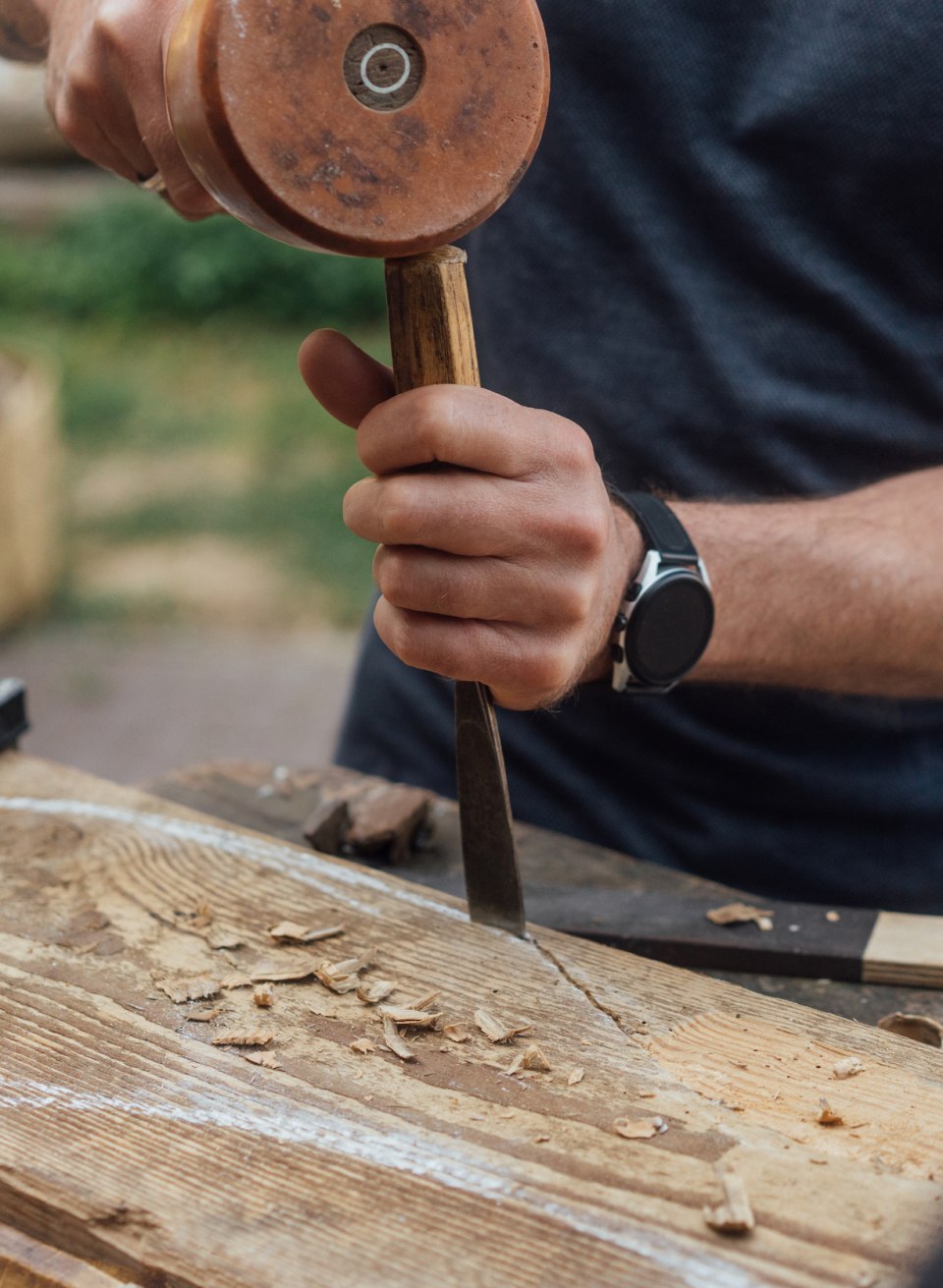 Iemand boetseert iets in een groot stuk hout met een hamer en beitel tijdens de workshop beeldhouwen