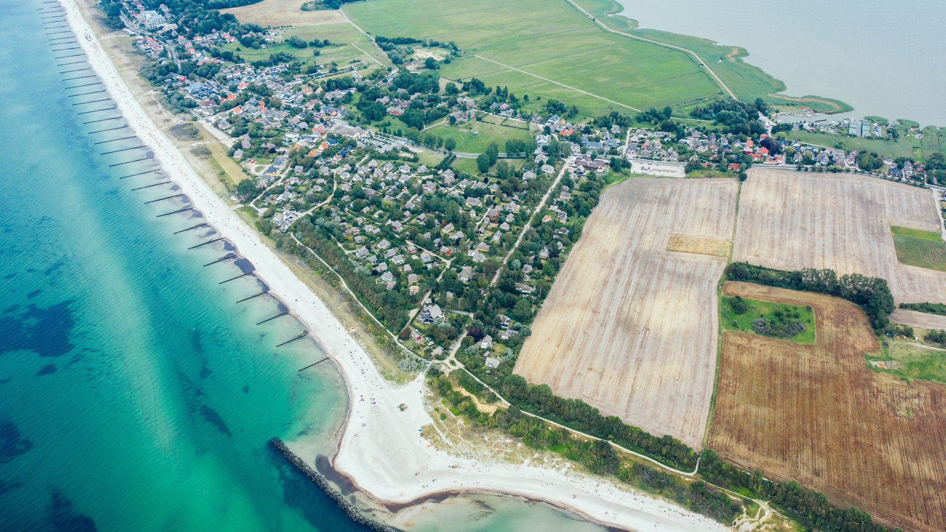 Aerial view of a coastal landscape on Rügen with beach, fields, green meadows and clear turquoise Baltic Sea water. // Between the blue sea and golden fields - the coastal region of Fischland-Darss-Zingst combines nature, vastness and Nordic serenity in perfect harmony. // © MV-T/Gänsicke Aerial view of a coastal landscape on Rügen with beach, fields, green meadows and clear turquoise Baltic Sea water.