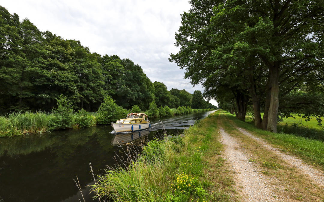 A boat glides along quiet canals in the Lewitz past rows of green trees. A narrow path along the water invites you to explore slowly - Mecklenburg nature to take a deep breath, Friedrichsmoor included. // &copy; MV-T/Gohlke