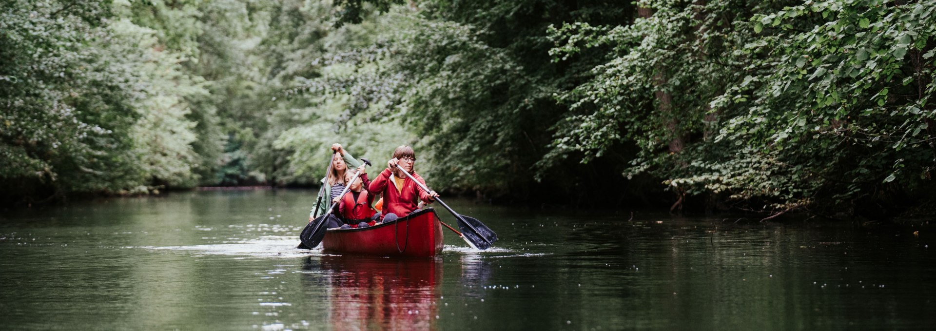 Twee mensen peddelen in een rode kano door een met bomen omzoomde rivier in het M&uuml;ritz National Park.