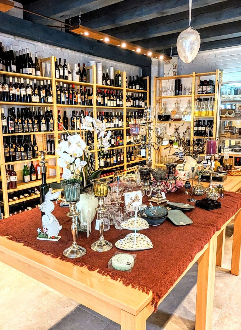 Interieur van de wijnwinkel "Weinhaus im Hof" met schappen vol wijnflessen, delicatessen en decoratieve cadeauartikelen.