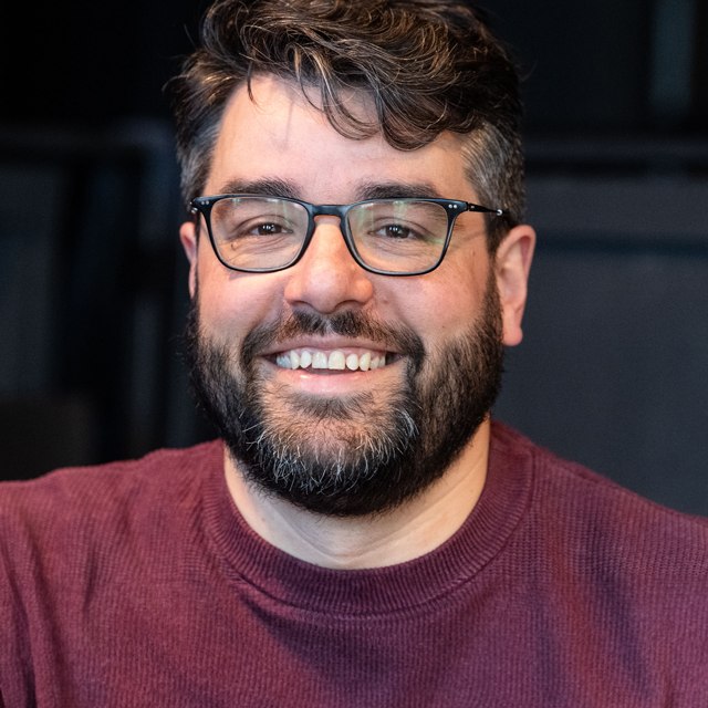 Portrait photo of assistant director Georg Meier in a wine-red sweater against a dark background., © Peter van Heesen
