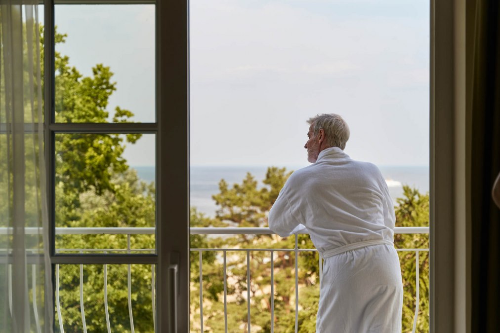 zimmer-mann-im-bademantel-auf-balkon-am-gelaender-strandidyll-heringsdorf, &copy; DSR Hotel Holding