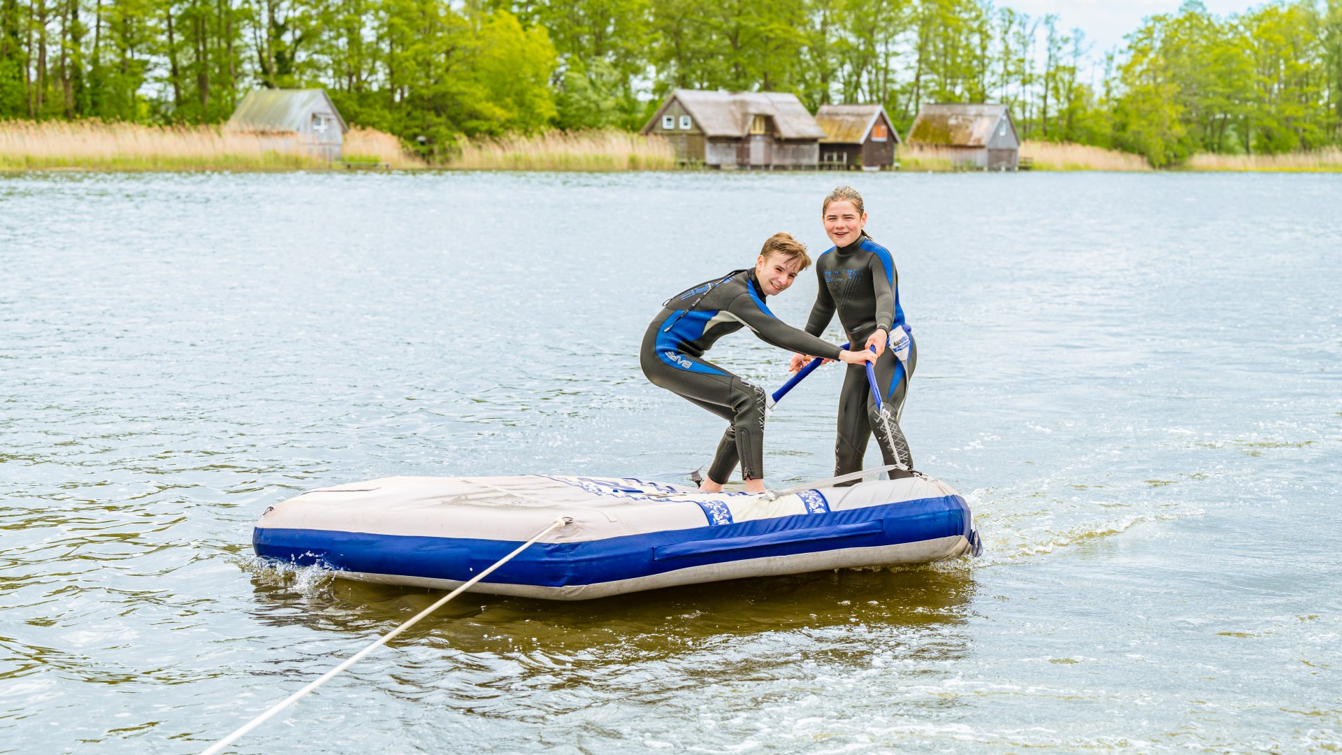 On the bathing island, Ferri and Theo let themselves be pulled across the lake. Who will manage to stay standing for longer?, © TMV/Tiemann Two children on a bathing island being towed behind a boat.