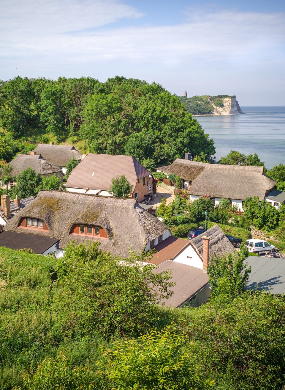The fishing village of Vitt on the island of Rügen with traditional thatched-roof houses, surrounded by green nature, with the cliffs of Cape Arkona and the Baltic Sea in the background.
