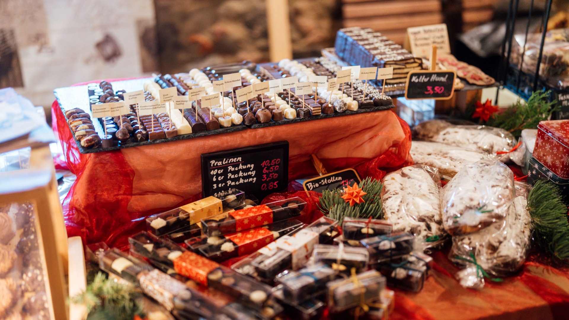 Een feestelijk versierde marktkraam met handgemaakte pralines, bonbons en kerststollen, omringd door kerstdecoraties.