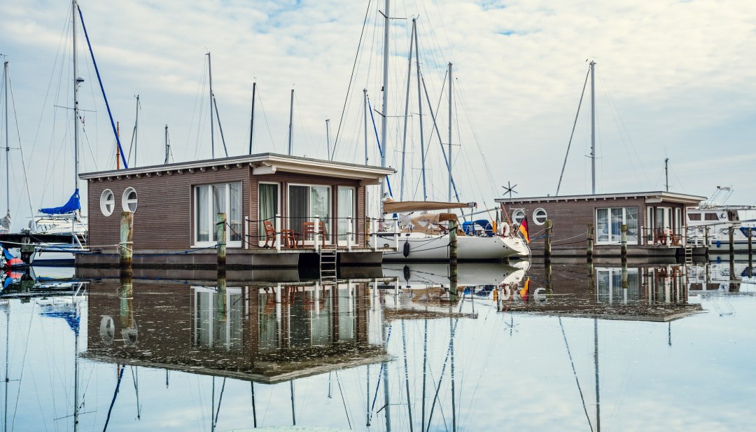 Drijvend vakantiegeluk: De suites, ontworpen in de stijl van woonboten, zijn stevig verankerd., © TMV/Tiemann Woonboten en zeilboten aangemeerd in de haven van Krummin