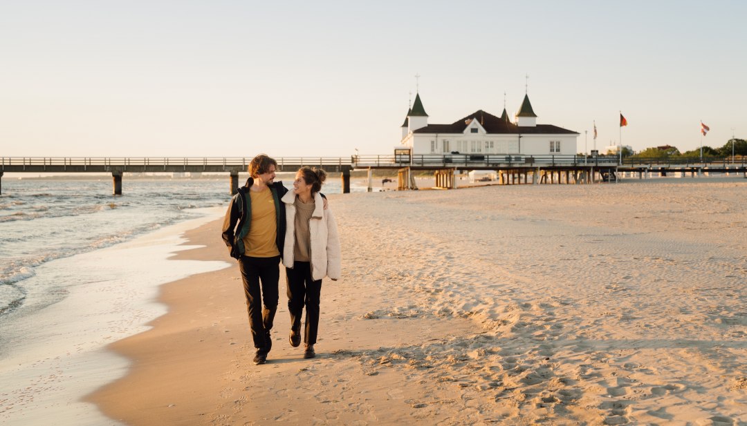 Paar wandelt langs de historische pier op Usedom bij zonsondergang op het strand van de Baltische Zee in Ahlbeck.