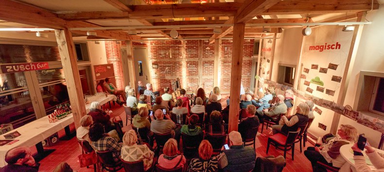 People sit in the illuminated coach house and look towards the stage // © Oliver Borchert People sit in the illuminated coach house and look towards the stage // © Oliver Borchert