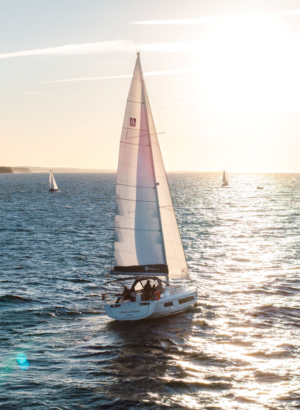 Zeilboot met wit zeil op de Oostzee bij Warnem&uuml;nde bij zonsondergang met glinsterend water.