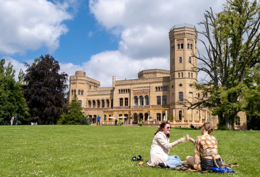 Two women enjoy a picnic on a meadow in front of Neetzow Castle on a sunny day during the Midsummer Remise.