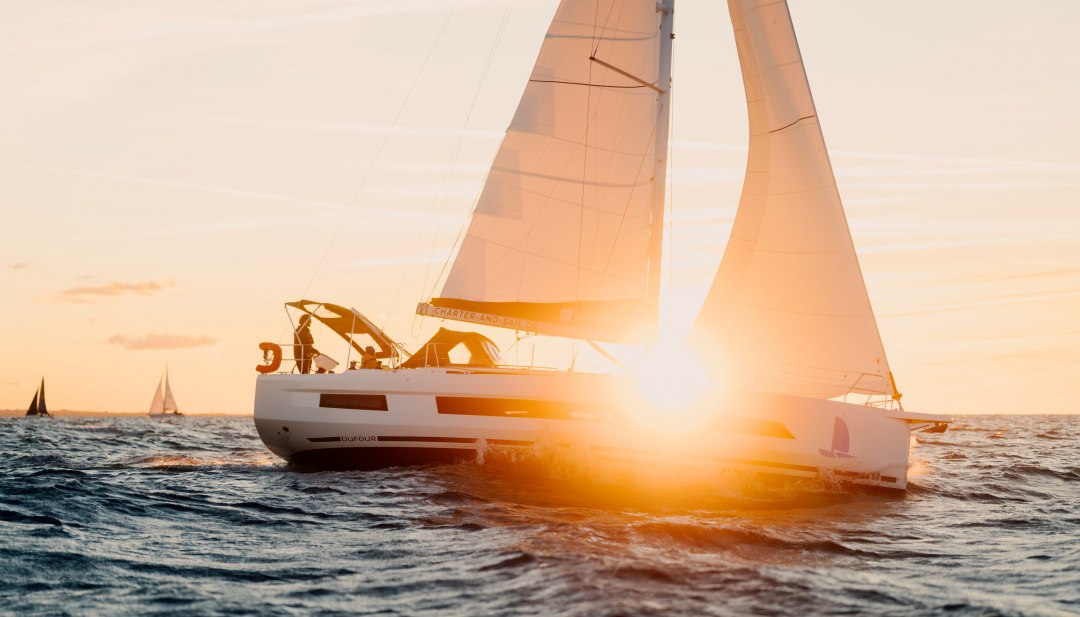 Zeilboot met oranjekleurige zeilen op de Oostzee bij Warnem&uuml;nde bij zonsondergang.