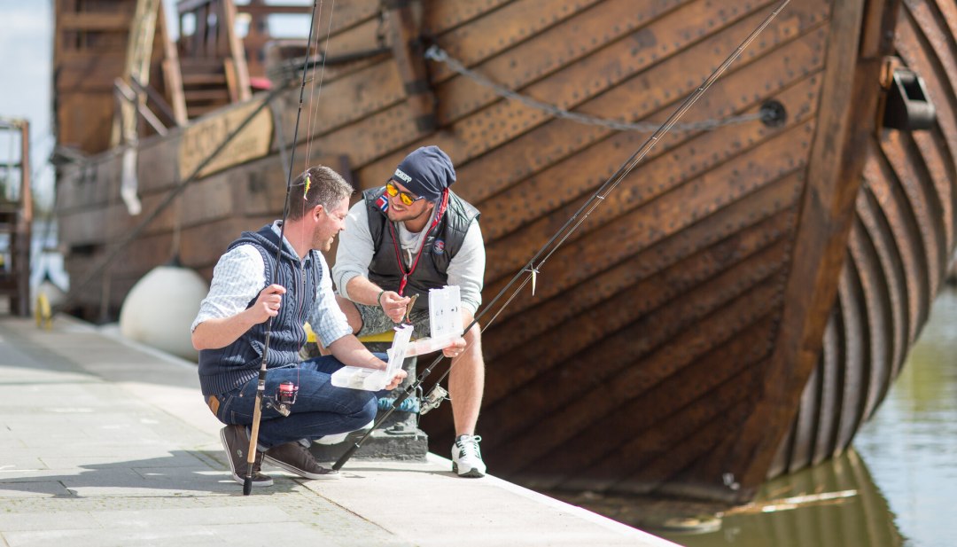 Jonge mannen vissen in de haven van Ueckermünde met een tandrad op de achtergrond., © TMV/Läufer