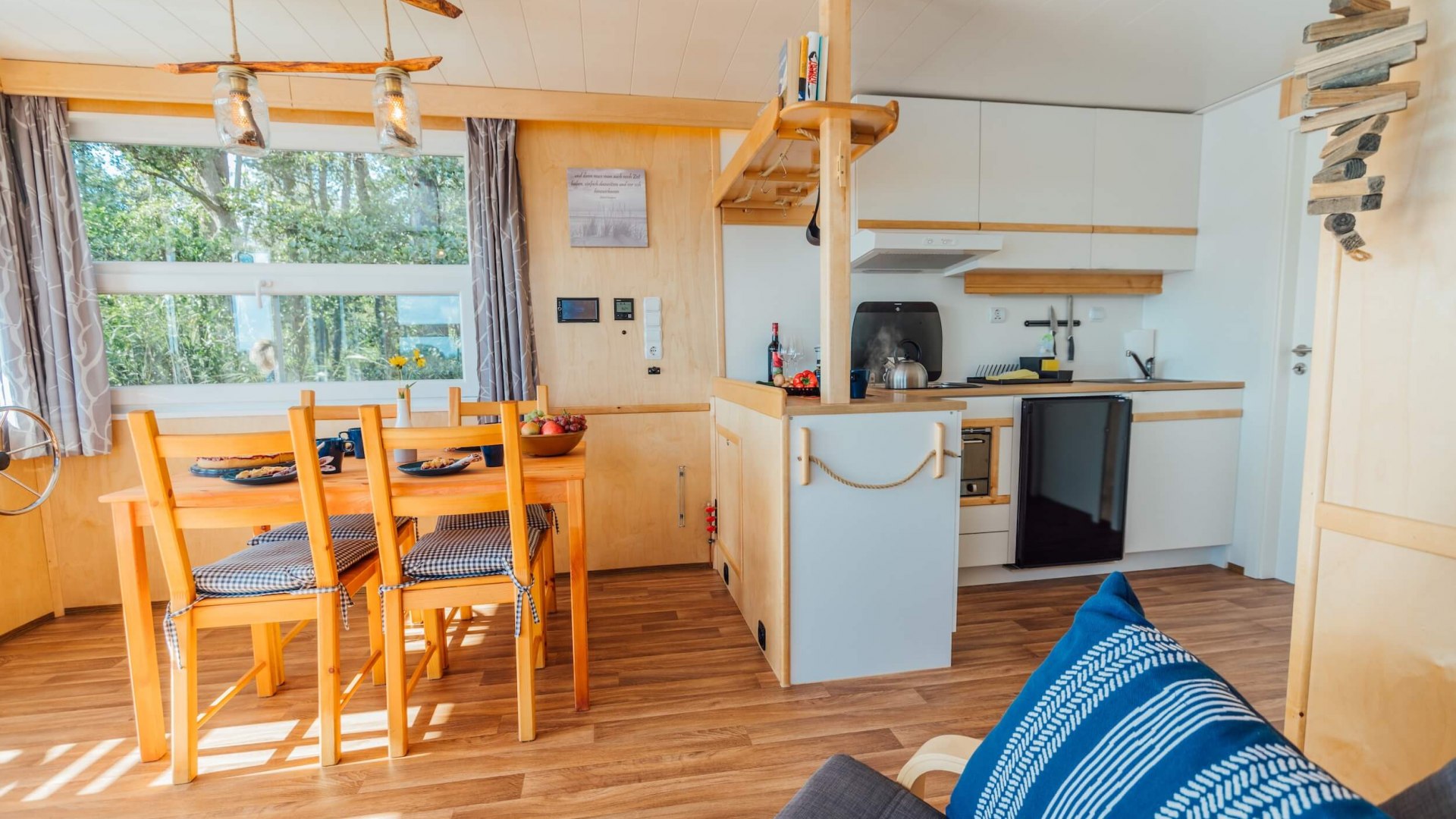Gezellige woon- en eetruimte van een woonboot op de Peene, uitgerust met een moderne keuken en een warme, uitnodigende sfeer., © Abenteuer Flusslandschaft Interieur van een woonboot op de Peene met eethoek, keuken en gezellige inrichting.