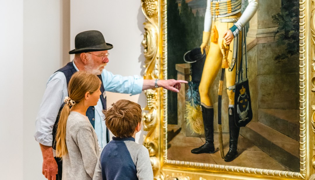 De rondleiding voor kinderen toont het schilderij van Prins Wilhelm Malte I en twee kinderen zijn verbaasd. // "Kijk eens naar het uniform! " De kinderen leren dat Prins Wilhelm Malte I Zweeds geel draagt. // © MV-T/Tiemann De rondleiding voor kinderen toont het schilderij van Prins Wilhelm Malte I en twee kinderen zijn verbaasd.