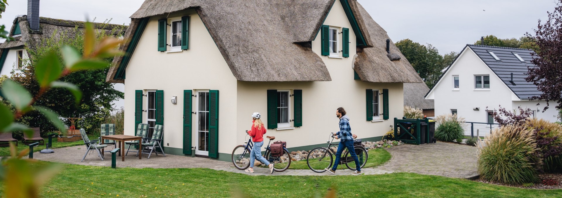 A couple with bicycles in front of a charming thatched-roof vacation home on the island of Poel.