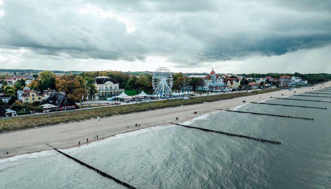 Widok z lotu ptaka na nadmorską promenadę w K&uuml;hlungsborn nad Morzem Bałtyckim z piaszczystą plażą, ostrogami, diabelskim młynem i zabytkowymi budynkami w tle.