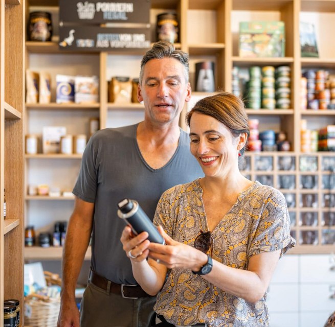 Smiling couple in a farm store, surrounded by shelves of regional products, examining an item.