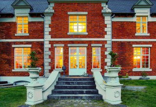 Illuminierter Eingang des Herrenhauses Brookhusen: Historistische Backsteinfassade und einladend leuchtende Fenster in der Abendd&auml;mmerung. // &copy; Herrenhaus Brockhusen