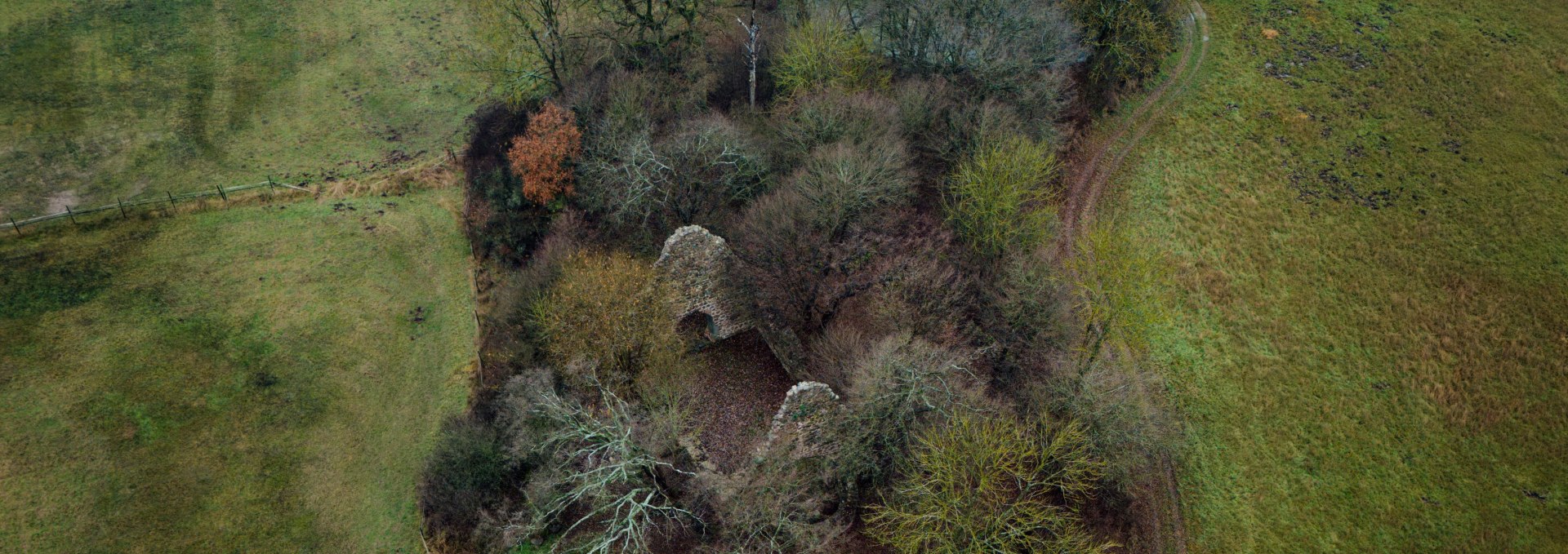 Aerial view of the "Wüste Kirche" ruins near Penzlin, surrounded by trees, meadows and a winding path.